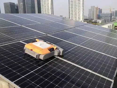 A robotic cleaner moving across solar panels on a city rooftop