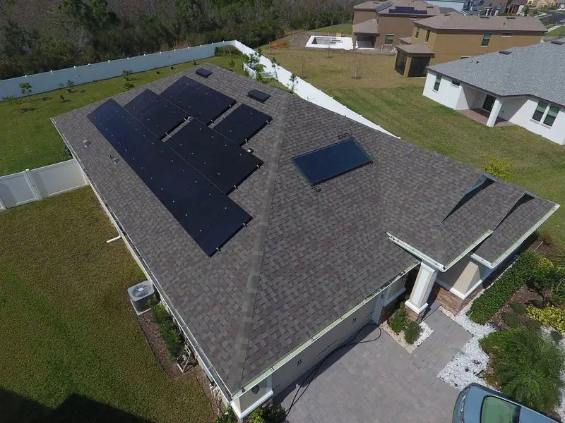 Aerial view of a home with a large rooftop solar array and a fenced backyard