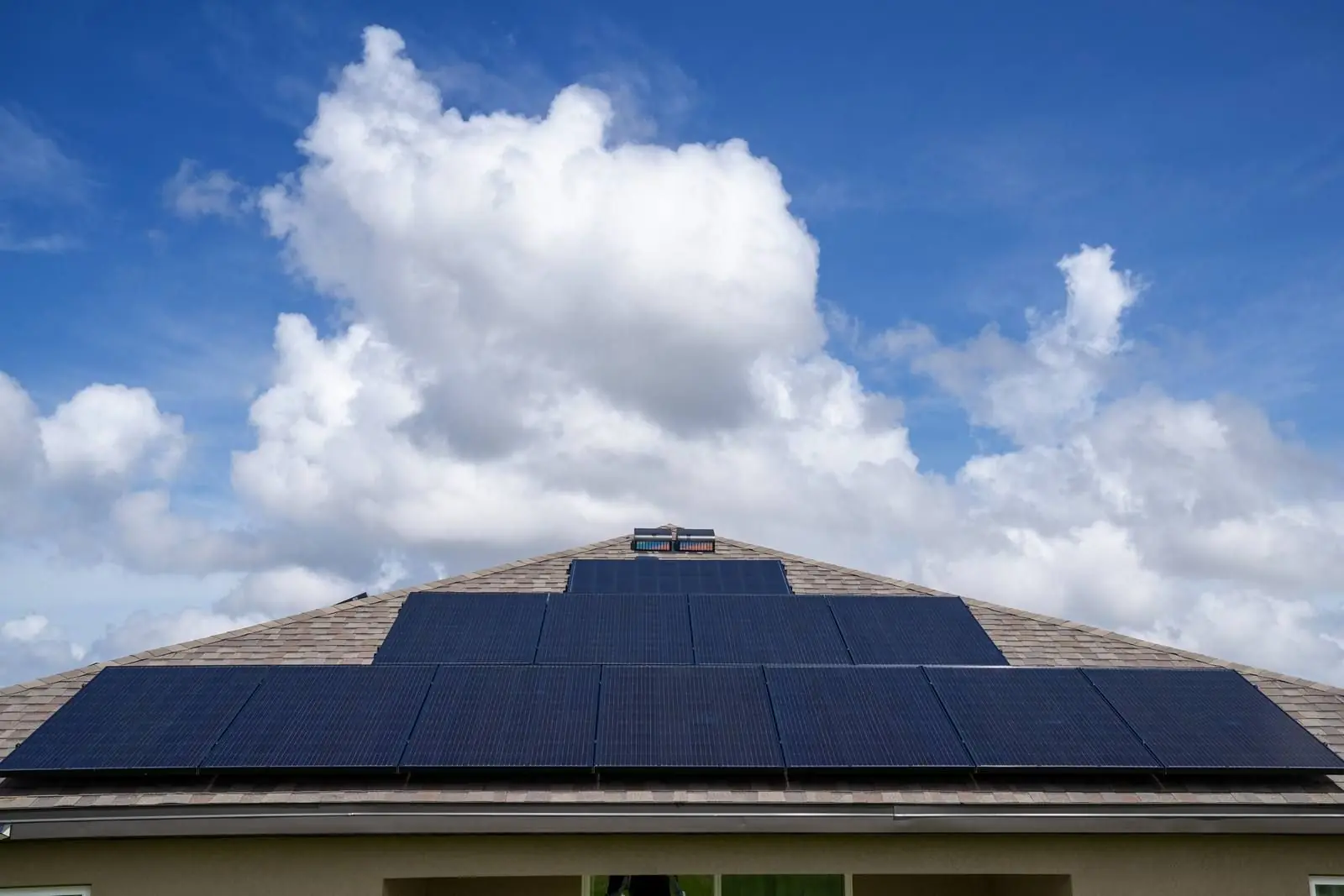 Solar panel array on a residential roof under a blue sky with white clouds