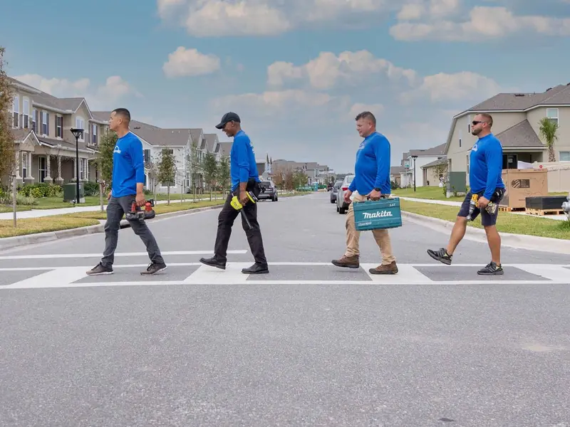 Four Solar Sage installers in blue company shirts crossing a residential street with their tools